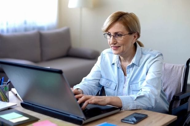 Kobieta na wózku pracująca przy laptopie.