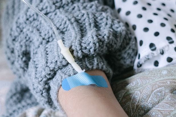 Fragment ręki, do której podłączona jest kroplówka.