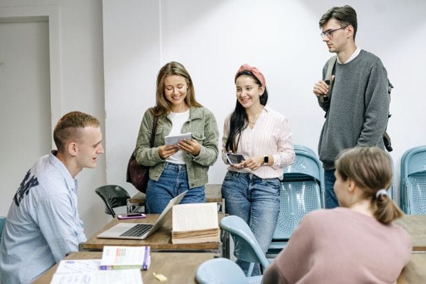 Młodzi ludzie, studenci. W sali uczelnianej rozmawiają ze sobą.
