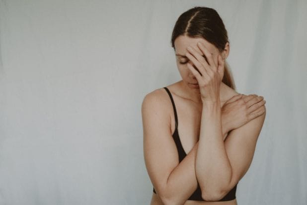 Kobieta. Prawą rękę położoną ma na lewym ramieniu. Lewą ręką zakrywa częściowo twarz. Ma pochyloną głowę, zamknięte oczy.