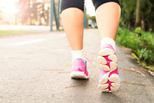 Ukazane nogi od kolan w dół biegnącej kobiety. Na stopach ma biało-różowe buty sportowe.