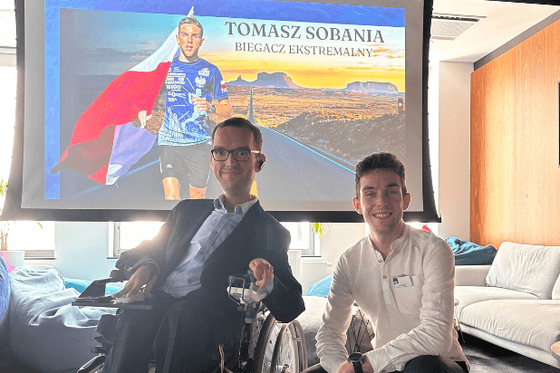 Tomasz Sobania i Adrian Furman na tle ekranu ze zdjęciem biegnącego Tomasza Sobani z flagą Polski