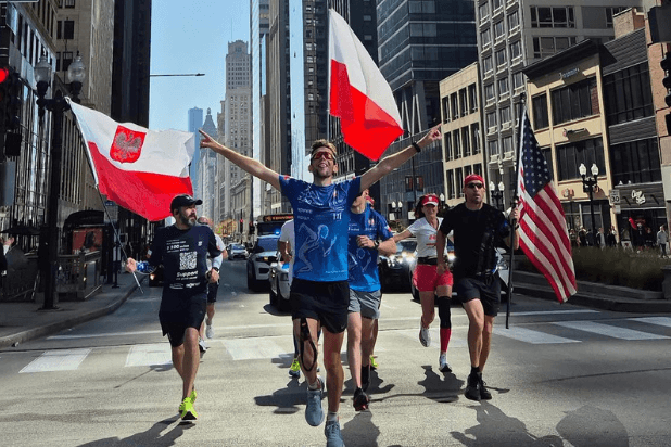 Tomasz Sobania w towarzystwie kilku biegaczy biegnie z polską flagą w Chicago. Jeden z biegaczy trzyma również polską flagę, inny biegacz trzyma flagę amerykańską